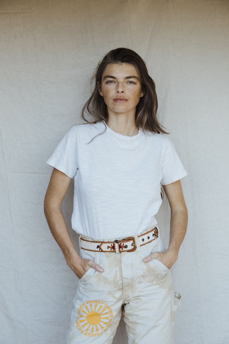 Woman with freckles standing against a plain background with hands in pocket